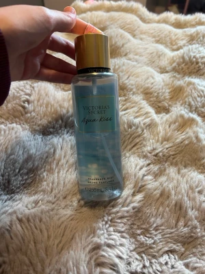 Victoria's Secret Aqua Kiss mist - Fräsch body mist från Victoria's Secret i doften Aqua Kiss. Flaskan är genomskinlig med blått innehåll och har ett guldfärgat lock. Rymmer 250 ml och har en elegant, enkel design med etikett i blått och guld. Perfekt för dig som gillar lätta, fräscha dofter.