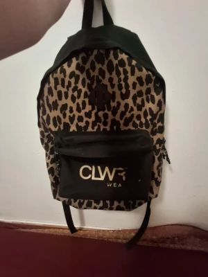 Leopardmönstrad ryggsäck CLWR - Snygg ryggsäck från CLWR med leopardmönstrad framsida och svart baksida. Stor ytterficka med CLWR-logga i vitt och dragkedja. Justerbara axelband och praktiskt bärhandtag upptill. Tillverkad i slitstarkt tyg, perfekt för skolan eller stan.