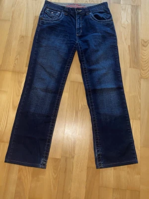 Mörkblå bootcut jeans - Snygga mörkblå bootcut jeans med slitningar framtill och bakfickor med dekorativa sömmar. Klassisk femficksmodell och normal midja. Perfekta till en avslappnad stil och passar till det mesta. Tillverkade i denim med lätt stretch. 34/32 midjemått 43cm