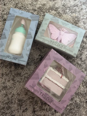 Cry Baby's Trilogy prydnadsset - Säljer ett set med tre prydnader från Melanie Martinez Cry Baby's Trilogy: en babyflaska i vitt och mintgrönt, en ljusrosa fjäril och en rosa jordgubbstårta. Alla kommer i originalkartong med söta motiv och fönster på framsidan.