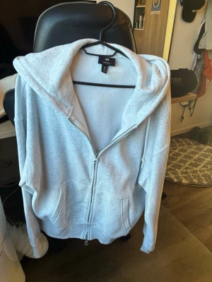Ljusgrå oversized hoodie från H&M - Säljer en ljusgrå hoodie från H&M i oversized fit. Hoodien har dragkedja framtill, stor huva och två rymliga fickor. Perfekt för en chill och avslappnad stil. Tillverkad i mjukt material som känns skönt mot huden.
