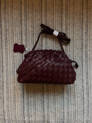 Mörkröd flätad handväska - Snygg mörkröd handväska med flätad design och justerbar axelrem. Väskan har en unik form med dragsko på sidorna. Perfekt för dig som vill ha en trendig accessoar med det lilla extra.