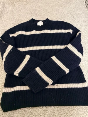 Svartvit randig stickad tröja H&M - Säljer en svart stickad tröja från H&M med vita horisontella ränder. Tröjan har ribbstickad struktur, rund halsringning och långa ärmar. Perfekt för dig som gillar klassisk och enkel stil.