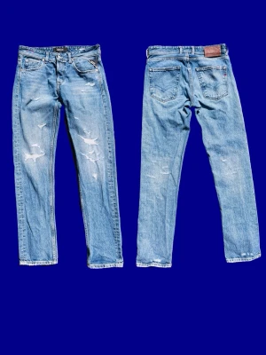 Ljusblå slitna jeans från Replay - Säljer ett par ljusblå jeans från Replay med raka ben och slitna detaljer på både fram- och baksida. Klassisk femficksmodell i denim med läderpatch bak i midjan och broderad detalj på bakfickan. Perfekta för en avslappnad och trendig look. W29 L32
