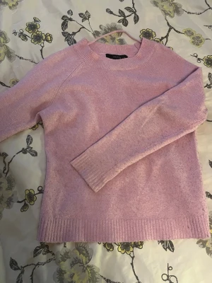 Ljusrosa stickad tröja Vero Moda - Mysig ljusrosa stickad tröja från Vero Moda i storlek XS. Tröjan har rund halsringning, långa ärmar och ribbade muddar vid ärmslut och nederkant. Perfekt för att hålla värmen under kyliga dagar. Lite noprig 