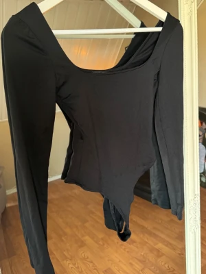 Svart långärmad body - Snygg svart body med långa ärmar och rundad urringning. Tillverkad i ett stretchigt och mjukt material som sitter tight mot kroppen. Perfekt att styla med jeans eller kjol för en clean look.