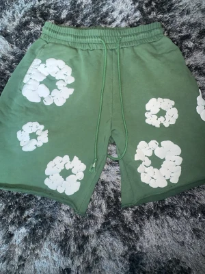 Gröna Denim Tears shorts - Säljer ett par gröna denim tears shorts med snörning i midjan. Shortsen har avslappnad passform och elastisk midja för extra komfort. Perfekta för varma dagar och chill stunder.