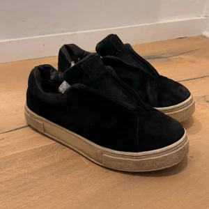 Svarta Eytys doja - Svarta slip-on sneakers med tjock vit sula och minimalistisk design. Ovandelen är i mockaliknande material utan synliga snören, vilket ger en clean look. Passar perfekt till streetwear och avslappnade outfits.
