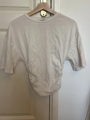 Vit croppad t-shirt med rynk - En vit croppad t-shirt med rynkade sidor och rund hals. T-shirten har korta ärmar och är gjord i mjuk bomull. Perfekt för en avslappnad och trendig look.