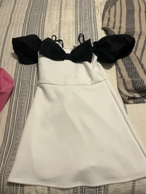 Vit klänning med svarta puffärmar - Superfin vit klänning från SHEIN med svarta puffärmar och en söt svart rosett framtill. Klänningen har axelband och en kort, utsvängd modell som ger en trendig look. Perfekt för dig som vill sticka ut med en unik och lekfull stil.