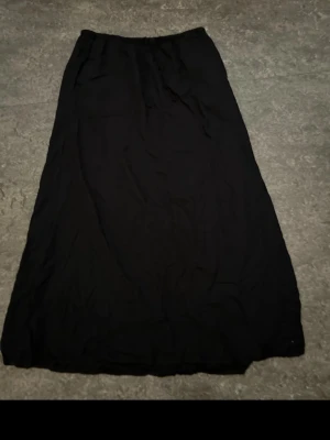 Svart långkjol i bomull - En enkel och stilren svart långkjol med rak passform. Kjolen har resår i midjan och är gjord i ett mjukt bomullstyg som känns bekvämt mot huden. Perfekt att matcha med en crop top eller stickad tröja.