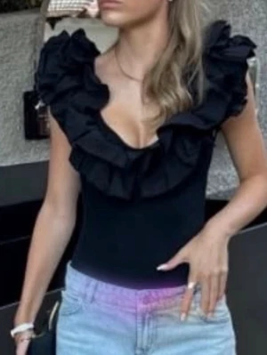 Svart topp med volangkrage - Trendig svart topp med djup urringning och stora volanger runt halsen. Figurnära passform och ärmlös design som ger en cool och chic look. Perfekt att styla med jeans eller kjol för en snygg outfit.