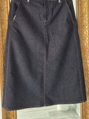 Mörkblå jeanskjol med fickor - Snygg mörkblå långkjol i denim med kontrastsömmar. Kjolen har två fickor fram och två bak. Ny oanvänd köpt för 1080kr