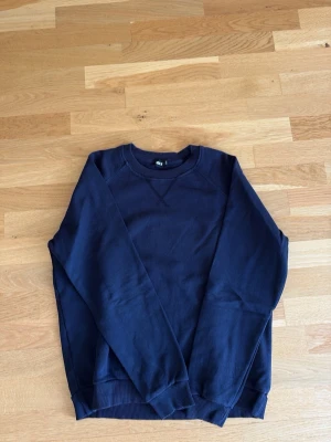Mörkblå sweatshirt med rund hals från RYVLS - En stilren mörkblå sweatshirt med rund halsringning och ribbade muddar vid ärmslut och nederkant. Tröjan har en klassisk passform och är tillverkad i mjukt material, perfekt för en avslappnad look.