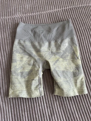 Grå camo träningstights shorts - Snygga gråa träningstights shorts med hög midja och camouflagemönster. Materialet är stretchigt och tight, perfekt för gymmet eller annan träning. De har en bred ribbad linning för extra komfort.
