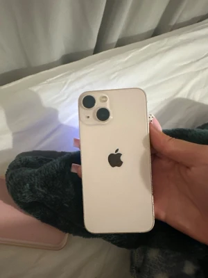 Rosa iphone 13 mini  - Säljer en vit iPhone med stilren design och rundade kanter. Telefonen har två stora kameralinser på baksidan och Apples logga i mitten. Skärmen är stor och täcker nästan hela framsidan med en liten notch upptill. Batterihälsam är på 88%. Lågt pris därav laddingsporten kan i vissa få fall glappa, kontakta vid frågor. Skal+skärmskydd ingår☺️