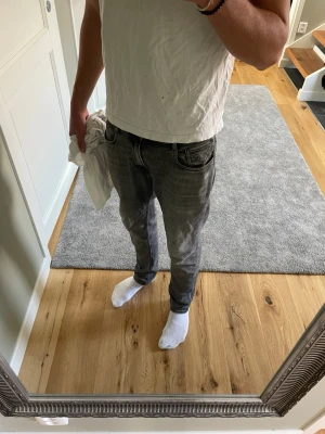 Grå slim fit jeans från Replay - Snygga grå slim fit jeans från Replay med klassisk femficksdesign och diskreta slitningar. De är 30 i midjan o 32 längd Jeansen har dragkedjegylf och svarta detaljer vid fickorna. Perfekta för en trendig och avslappnad look.