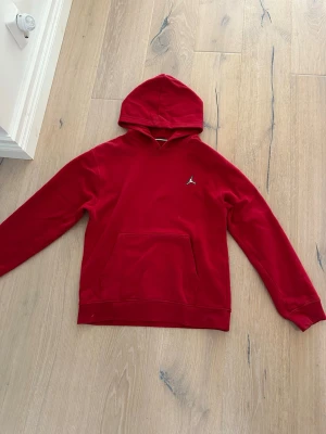 Jordan hoodie -  Röd Jordan hoodie med huva och klassisk känguruficka framtill. På bröstet sitter en liten vit Jordan-logga. Hoodien har ribbade muddar vid ärmslut och nederkant. Passar perfekt för dig som gillar streetwear och mode.