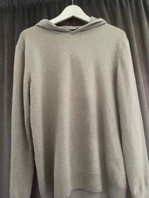 Beige hoodie från Oscar Jacobson - Mjuk och stilren beige hoodie från Oscar Jacobson. Tillverkad i Italien med lång ärm och ribbade muddar. Hoodien har en enkel design utan tryck eller dragkedja, perfekt för en clean och avslappnad look.