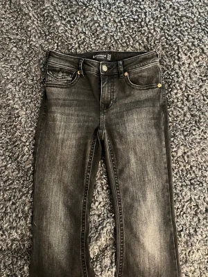 Svarta tvättade jeans från Stradivarius  - Snygga svarta jeans från Stradivarius med tvättad look och raka ben. Klassisk femficksmodell med silverfärgade nitar och knapp. Jeansen har en beige patch bak i midjan och är tillverkade i stretchigt denimtyg för skön passform.