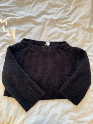 Svart croppad stickad tröja - En svart, croppad stickad tröja med rund hals och långa ärmar. Tröjan har en enkel och clean design som passar perfekt till jeans eller kjol. Materialet känns mjukt och bekvämt mot huden.