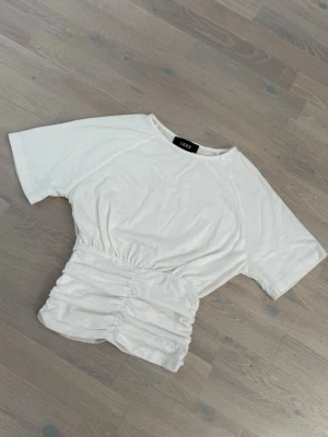 Vit topp med tight midja - Vit topp från cider med korta ärmar och rynkad tight midja. 