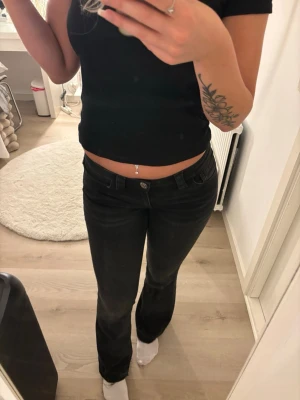 Svarta bootcut jeans med detaljer - Säljer ett par svarta bootcut jeans med snygga sömmar och dekorativa detaljer på bakfickorna. Jeansen har låg midja och klassisk femficksmodell. Perfekta för dig som gillar en stilren men ändå trendig look. Dom är uppsprättade längst ner.