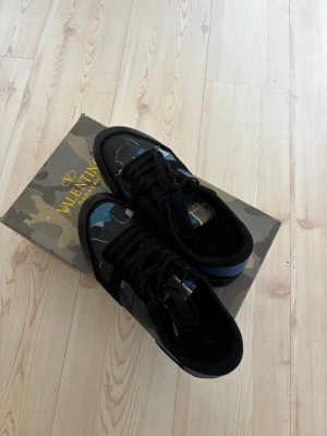 Valentiono rock runners - Valentino Rockrunner – Svarta – Storlek 42  Säljer ett par snygga Valentino Rockrunner sneakers i storlek 42. 🖤  Skorna är i svart med blå detaljer och säljs tillsammans med originalkartongen. Se bilder för exakt skick. Perfekta sneakers som passar både till vardags och en mer uppklädd outfit. 📩 Hör gärna av dig vid frågor eller om du vill ha fler bilder!