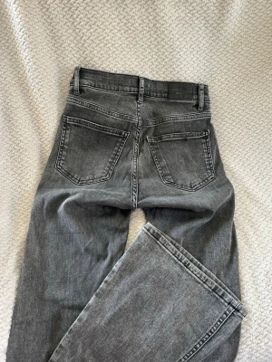 Gråa utsvängda jeans från Gina Tricot - Säljer ett par grå jeans från Gina Tricot med utsvängd passform och klassisk femficksdesign. Jeansen har normal midja, bälteshällor och stängs med knapp och dragkedja. Perfekta till en avslappnad och trendig look.