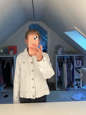 Vit jeansjacka med silverknappar - Snygg vit jeansjacka med klassisk krage och silverfärgade knappar framtill. Två bröstfickor med lock och knapp, samt raka ärmar. Perfekt att slänga över en t-shirt för en fräsch look. Passar till det mesta och ger en clean vibe.