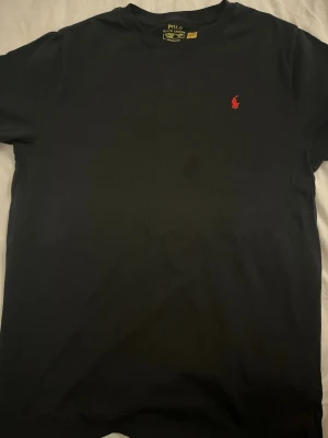 Svart Ralph lauren t-shirt - Äkta svart Polo Ralph Lauren T-shirt i 100% bomull.  Storlek: Youth XL, 170/88 (18–20 år).  Endast använd en gång och är i princip som ny. Det finns en liten mörk fläck framtill som knappt syns, se bilder. I övrigt är T-shirten i mycket fint skick utan hål eller andra skador.  Tvättlappen på insidan är bortklippt, men storleks- och Ralph Lauren-märkningen finns kvar. Fler bilder eller mått kan skickas vid intresse.