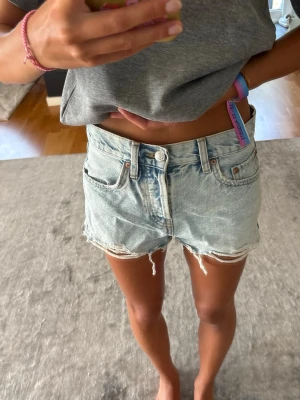 Ljusblå jeansshorts  - Ljusblå jeansshorts med slitningar och knapp gylf. 
