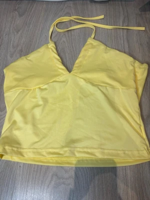 Gul halterneck topp  - Snygg gul halterneck topp från SHEIN i mjuk och stretchig polyesterblandning. Toppen har en v-ringad skärning och knytband i nacken, perfekt för sommarens alla outfits. Oanvänd 