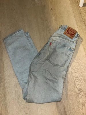 Ljusblå Levi's 501 jeans - Säljer ett par klassiska ljusblå Levi's 501 jeans med rak passform och hög midja. Jeansen har fem fickor, knappgylf och den ikoniska läderlappen bak i midjan. Perfekta för en avslappnad och trendig look.
