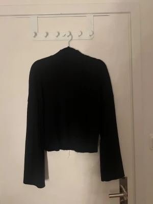 Svart croppad stickad tröja - En svart croppad stickad tröja med långa ärmar och enkel design. Perfekt för att matcha med höga jeans eller kjol. Tröjan har en rak passform och mjukt material som känns skönt mot huden.