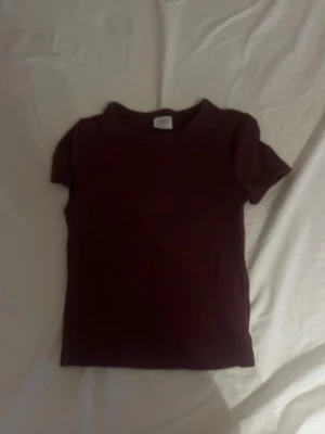 Mörkröd basic t-shirt - En enkel mörkröd t-shirt med rund hals och korta ärmar. Modellen är rak och klassisk, perfekt för en clean och stilren look. Materialet ser ut att vara mjukt bomullstyg som känns skönt mot huden.