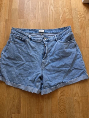 Blå denimshorts från ONLY - Säljer ett par klassiska blå denimshorts från ONLY i storlek XL. Shortsen har hög midja, fem fickor, knapp och dragkedja framtill samt uppvikta benslut. Perfekta för varma dagar och enkel att matcha med allt.