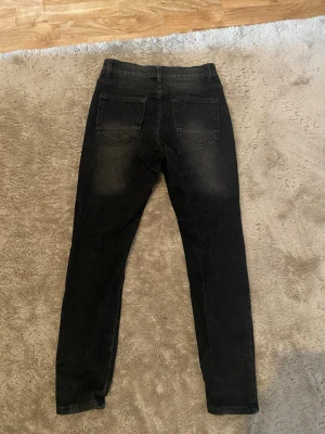 Svarta skinny jeans med slitningar - Säljer ett par svarta skinny jeans med lätt slitna detaljer och klassisk femficksmodell. Jeansen har hög midja och smal passform hela vägen ner. Materialet är stretchigt för extra komfort och sitter snyggt på benen.