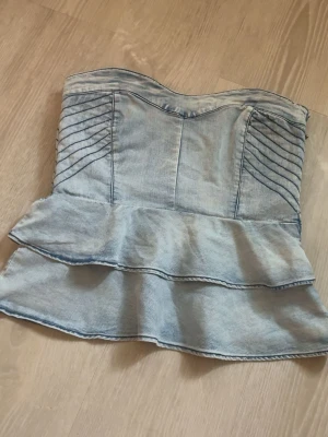 Ljusblå jeans tubtopp med volang - säljer en snygg tuntopp, jätte söt nu till hösten för man kan ha en kofta över !! väldigt unik och söt