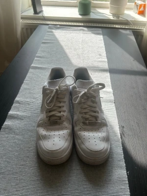 Air Force 1 - Säljer ett par vita sneakers med lågt skaft och snörning. Skorna har en stilren design med perforerade detaljer på tån och en tjock sula. Passar perfekt till jeans eller shorts för en clean och enkel look.