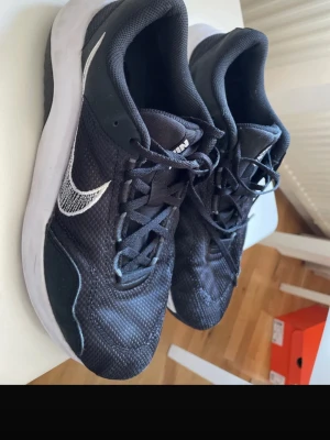 Svarta Nike sneakers med vit sula - Säljer ett par svarta Nike sneakers med vit sula och vit swoosh på sidan. Skorna har mesh-överdel för bra ventilation och klassisk snörning. Perfekta för dig som gillar sportig och stilren look.