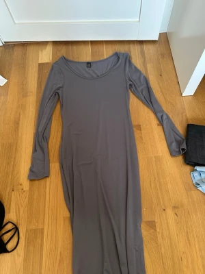 Grå långärmad långklänning - En enkel och stilren grå långklänning med lång ärm och rund halsringning. Klänningen har en rak passform och är tillverkad i ett mjukt, stretchigt material som ger en bekväm känsla.