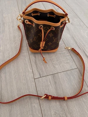 Louis Vuitton Monogram Bucket Bag - Snygg brun bucket bag från Louis Vuitton med klassiskt monogrammönster och detaljer i ljusbrunt läder. Väskan har justerbar axelrem, guldfärgade metalldetaljer och dragskostängning. Går endast ner i pris vid möte i göteborg