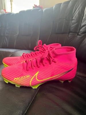 Fotbollsskor - Snygga fotbollsskor från Nike i en stark rosa färg med gula detaljer och svart swoosh. Skorna har inbyggd socka för extra stöd runt ankeln och snörning framtill. Yttersulan är gul med dobbar för bra grepp på planen. Perfekta för dig som vill sticka ut på matchen!