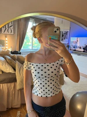 Vit offshoulder topp med svarta prickar - Säljer en söt offshoulder topp i vitt med svarta prickar. Toppen är croppad och har en tight passform som framhäver midjan. Perfekt till sommaren och ger en fräsch look. Materialet känns mjukt och stretchigt, troligen bomull eller polyester.