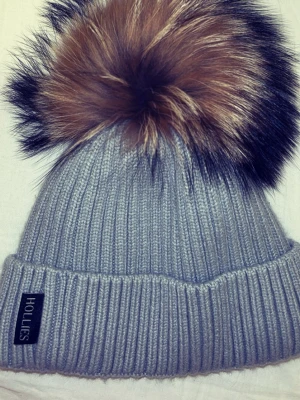 Hollies mössa - Mössan är helt ny och har aldrig använts innan. Mössan har uppvikt kant och mjukt vitt fleecefoder på insidan för extra värme. Perfekt accessoar för kalla dagar. Och en jätte söt fluffig pälsboll!!