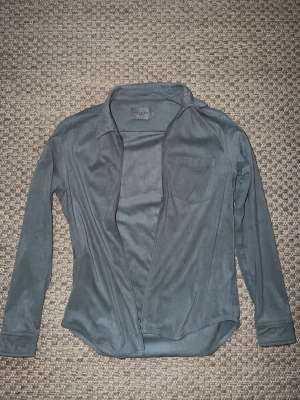 Blå skjorta i mocka från Velour - Snygg blå skjorta i mjuk mocka från Velour. Skjortan har lång ärm, klassisk krage, bröstficka och stängs med dragkedja framtill. Perfekt för dig som vill ha en stilren och modern look.