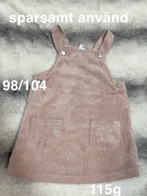 Rosa manchesterkjol med hängslen - Supersöt rosa manchesterkjol med hängslen och två framfickor. Kjolen har knappar på axelbanden och sidan för enkel påklädning. Perfekt för att styla med en t-shirt eller tröja för en trendig look.🌸 Sparsamt använd. Storlek 98/104