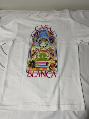 Vit Casa Blanca t-shirt med tryck - Vit t-shirt från Casa Blanca med färgglatt grafiskt tryck på både bröstet och ryggen. Trycket har ett konstnärligt motiv med blommor och landskap, samt röd text. Klassisk passform och rund halsringning.