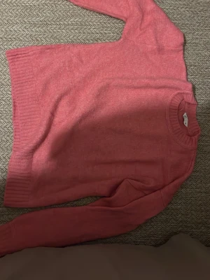 Rosa stickad tröja - Mysig rosa stickad tröja med rund halsringning och ribbade muddar vid ärmslut och nederkant. Perfekt för att hålla värmen under kyliga dagar och enkel att matcha med olika outfits.